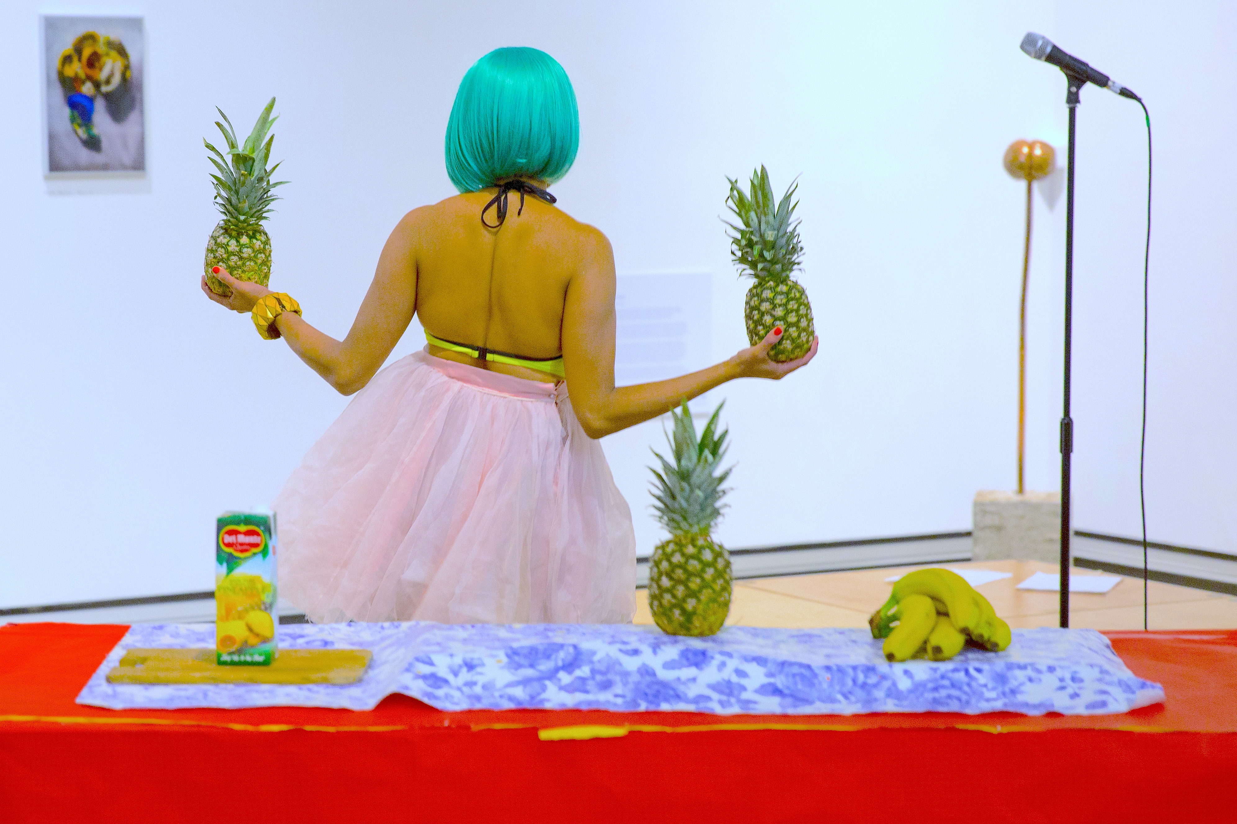Priya Mistry holds two pineapples in front of a colourful table