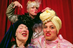 Three eccentric women take a selfie wearing makeup and brightly coloured outfits