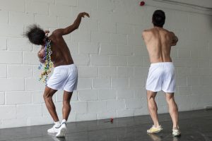 Two dancers wearing white shorts against a white brick background