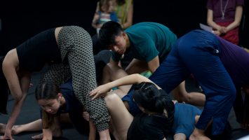 six dancers in dark clothes dancing, wrapping themselves around each other on the floor